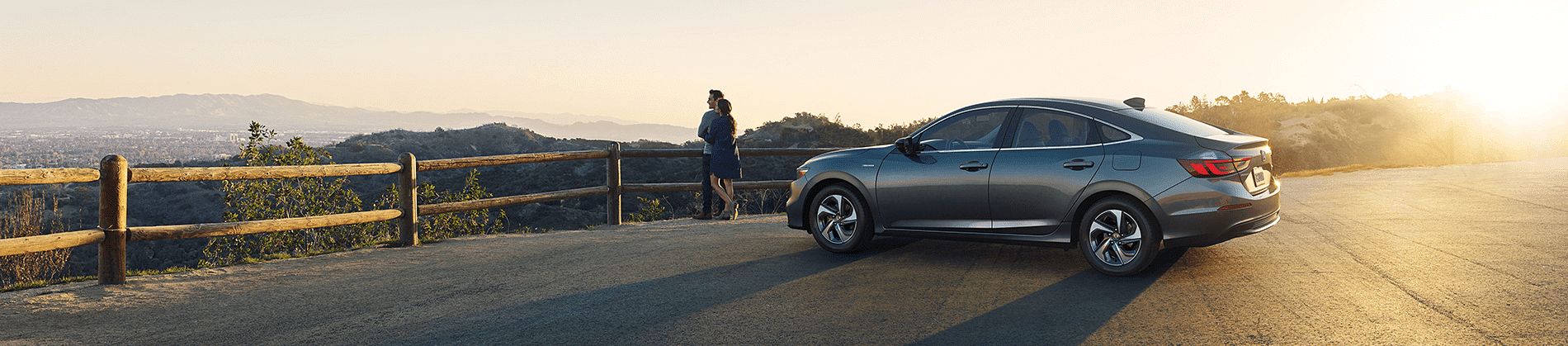 Honda car parked on the edge of a cliff and two people hugging each other admiring the views